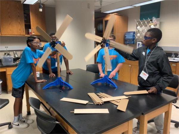 三个学生围着实验桌拿着螺旋桨叶片